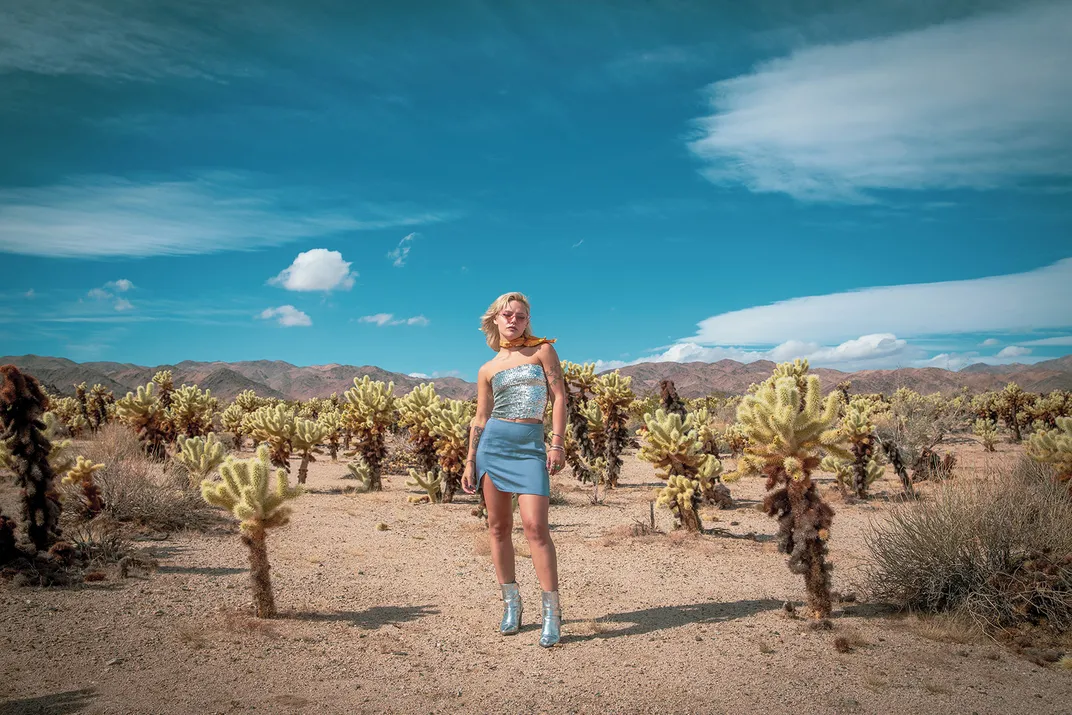 a women in a blue dress stands in the desert