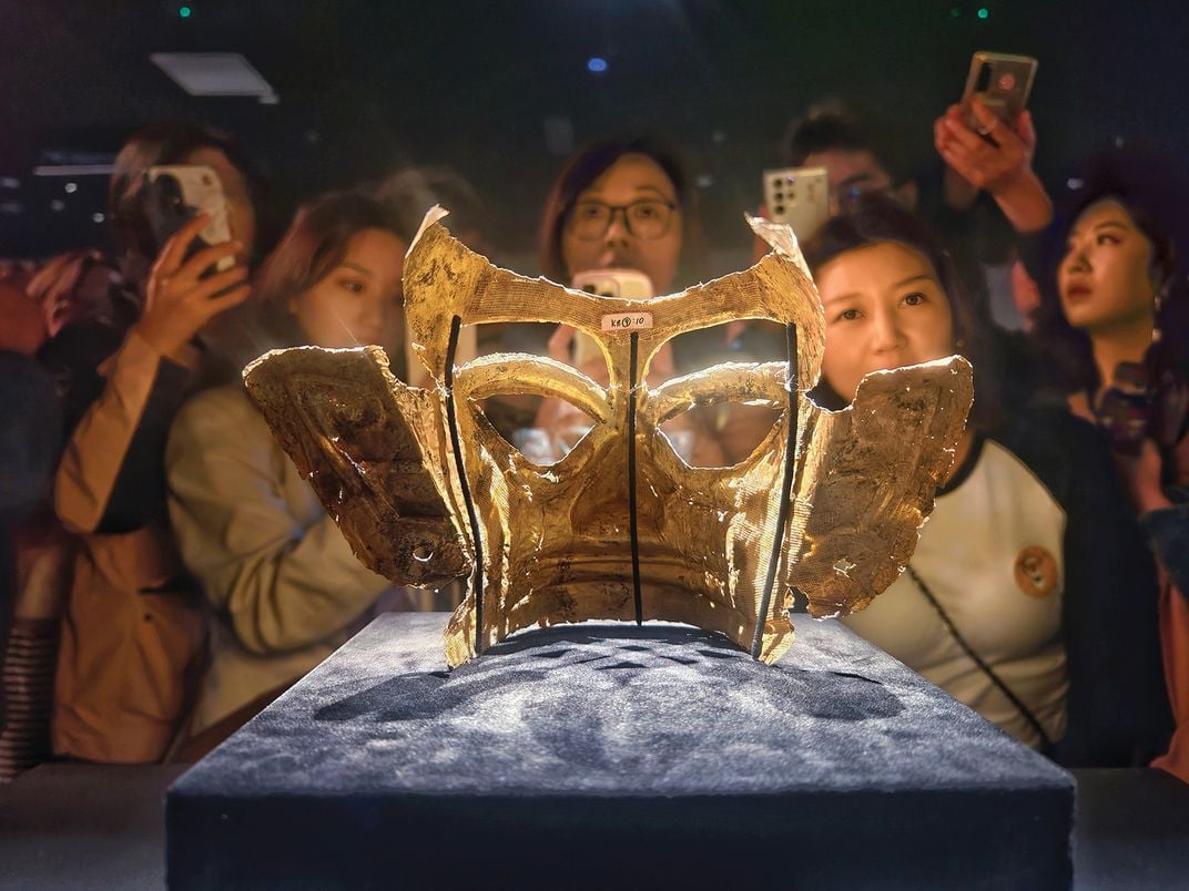 a group of museum visitors look at a golden mask that is behind glass