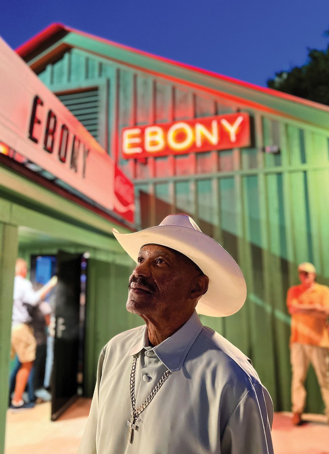 a man in a cowboy hat stands for a portrait outside of a nighclub