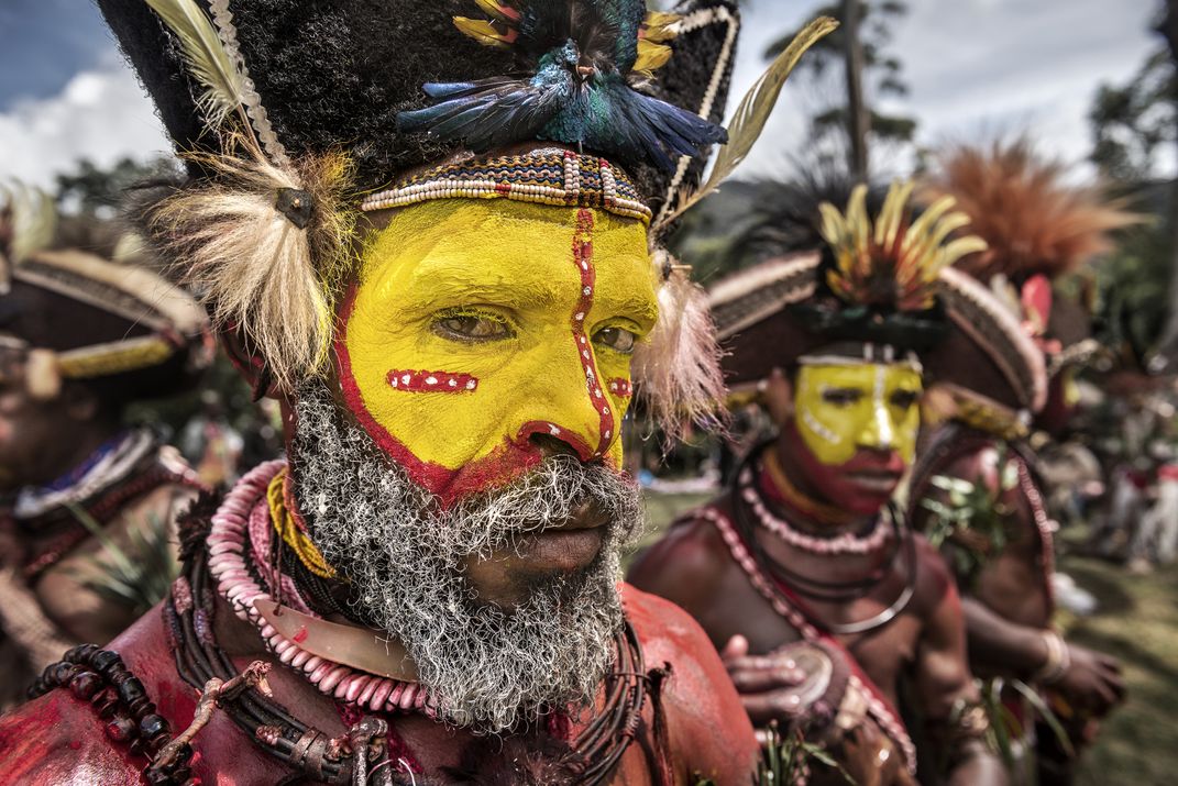 Huli Tribesmen with yellow face paint standing with other tribesmen