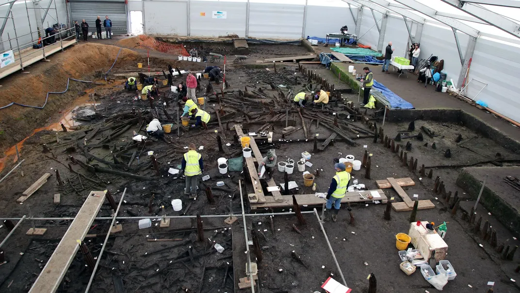 An excavation site enclosed in a building with people studying wooden remains